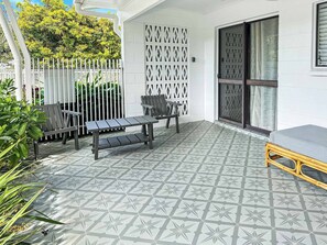 A patio with a patterned floor, a white fence, a bench, a table, and a sliding door.