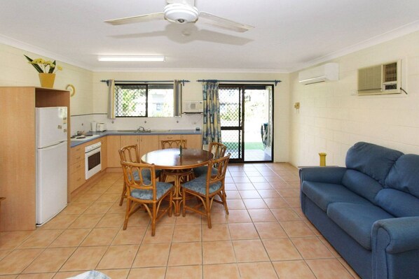 A compact kitchen with a dining table and chairs, a blue sofa, and a ceiling fan.