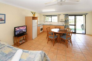 A compact kitchen with a dining area, a television on a stand, and a ceiling fan.