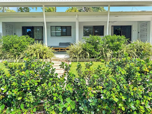A modern building with a covered walkway, surrounded by lush greenery and a clear sky.