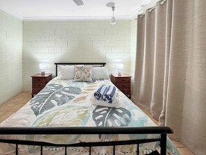 A bedroom with a bed, two bedside tables, a ceiling fan, and a window with curtains.