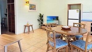 Un comedor con una mesa redonda, sillas de mimbre y piso de baldosas.