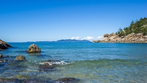 A coastal landscape with clear water, rocks, and a distant mountain range. - Alma Bay Holiday Unit 1 (Arcadia)