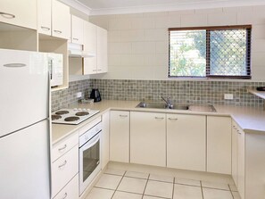 A kitchen with white cabinets, a stove, an oven, a sink, and a window with a view.