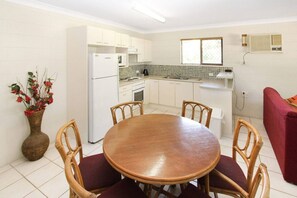 Cocina compacta con armarios blancos, refrigerador, microondas y pileta. Hay una mesa de comedor con cuatro sillas y un florero con flores rojas.