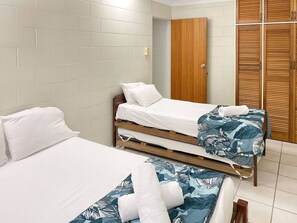 Habitación de hotel con dos camas, un armario de madera y una pared de azulejos blancos.