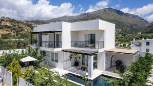 Une maison moderne à deux étages, dotée d’un balcon, d’une piscine et offrant une vue sur un paysage montagneux.