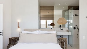 Une chambre moderne comprenant un lit, des tables de chevet, un miroir et un espace douche.
