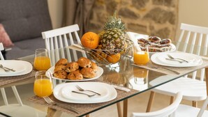 A breakfast setting with a glass table, white chairs, and a bowl of fruits and pastries. - Poseidon Apartments (Platanias)