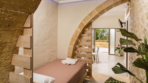 A bedroom with a wooden ladder, a bed with a white pillow, and a large arched doorway leading to a patio area. - Poseidon Apartments (Platanias)