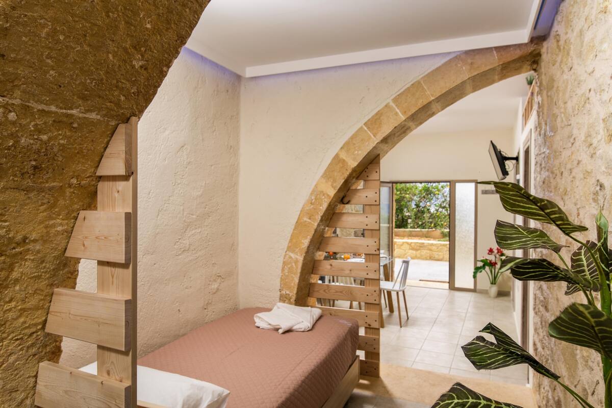 A bedroom with a wooden ladder, a bed with a white pillow, and a large arched doorway leading to a patio area.