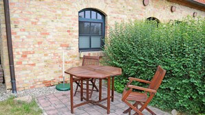 Un bâtiment en briques avec une fenêtre, une table et deux chaises à l’extérieur.