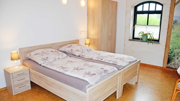 A bedroom with a bed, bedside tables, a wardrobe, a window with a plant, and a view of greenery. - 08 holiday apartment with terrace - holiday farm on Rügen (Putbus)