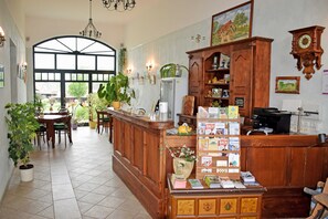 A reception area with a wooden counter, potted plants, a large window, and a wall clock. - 08 holiday apartment with terrace - holiday farm on Rügen (Putbus)