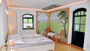 A bedroom with a bed, two chairs, a small table, and a window with a view of a landscape. - 08 holiday apartment with terrace - holiday farm on Rügen (Putbus)