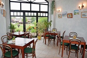 A dining area with wooden tables and chairs, potted plants, and artwork on the walls.