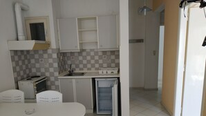 Cucina compatta con piano cottura, microonde e frigorifero. Si trova un tavolo da pranzo con sedie.