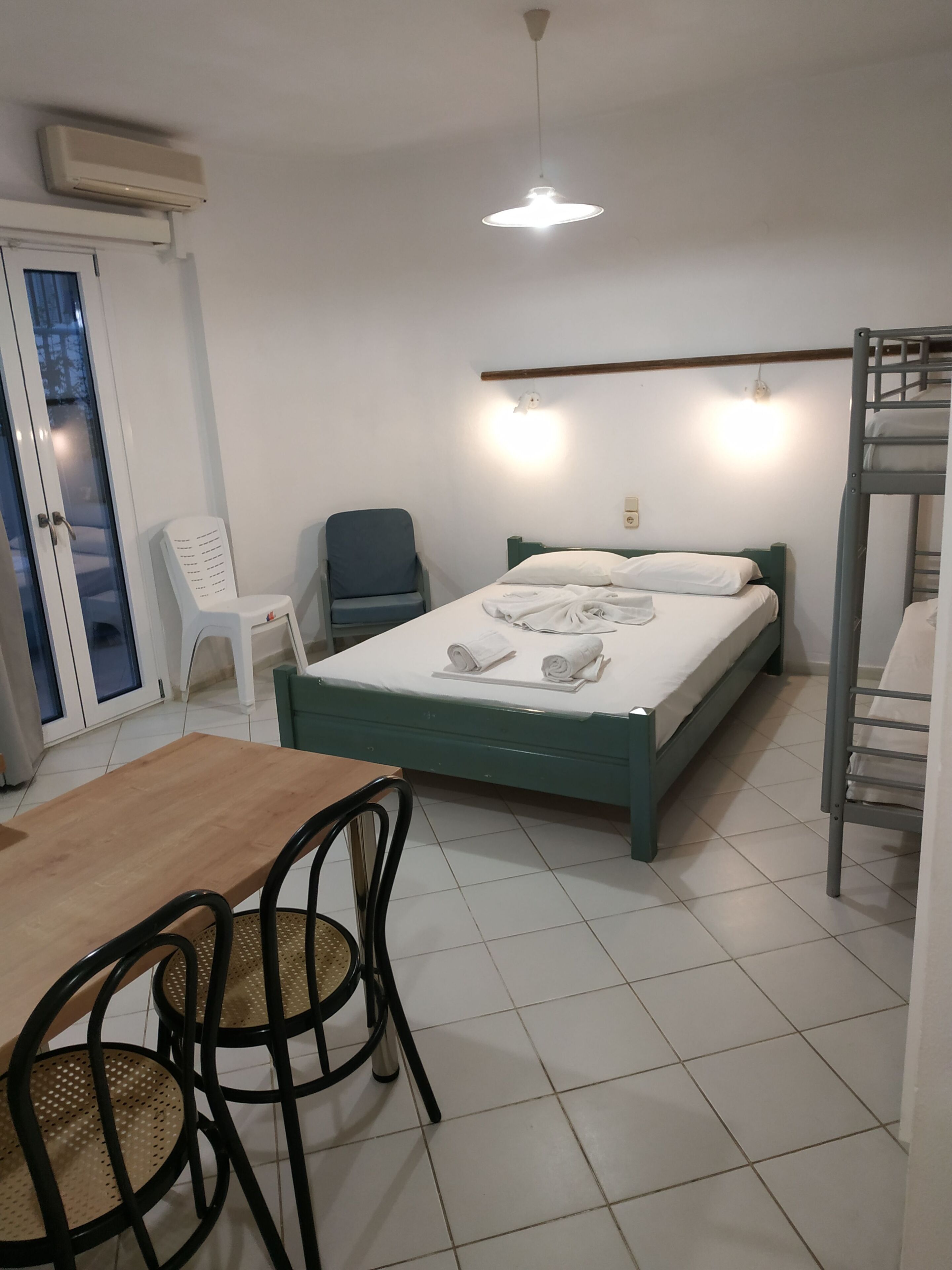 Habitació amb llit, taula, cadires, finestra i ventilador de sostre.