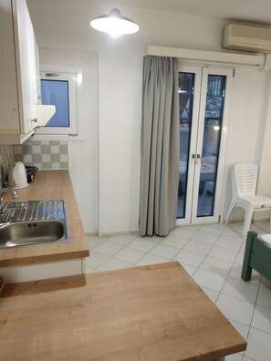 A kitchen with a sink, cabinets, a window, and a door with curtains. - Renia Studios Economy Studio Ground Floor (Malevizi)
