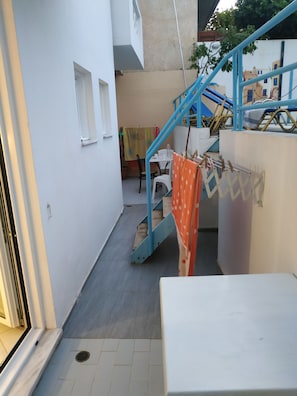 A narrow outdoor corridor with a blue staircase, a white table, and a chair. - Renia Studios Economy Studio Ground Floor (Malevizi)