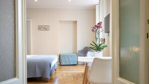 Habitación de hotel con dos camas, un escritorio, una silla, un radiador y una planta en maceta.