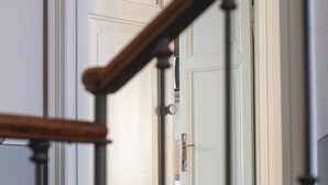 Una escalera con barandilla de madera que lleva a una puerta blanca con manija plateada.