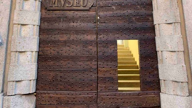 Una gran puerta de madera con la inscripción "MUSEO" y una escalera dorada que conduce a ella.