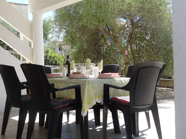 An outdoor dining area with a table set for four, surrounded by chairs, under a covered patio.