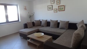 A living room with a sectional sofa, a coffee table, a window with blinds, and framed pictures on the wall.