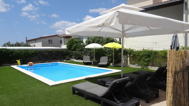 A swimming pool with a white pool cover, surrounded by artificial grass, and shaded by umbrellas.