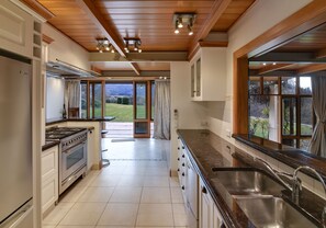 Cozinha com fogão, forno e pia. Há uma janela com vista para um jardim.