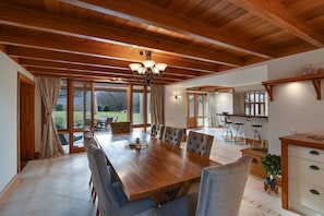 Uma ampla sala de jantar com uma grande mesa de madeira e assentos confortáveis, uma cozinha com eletrodomésticos modernos e grandes janelas com vista para o exterior.