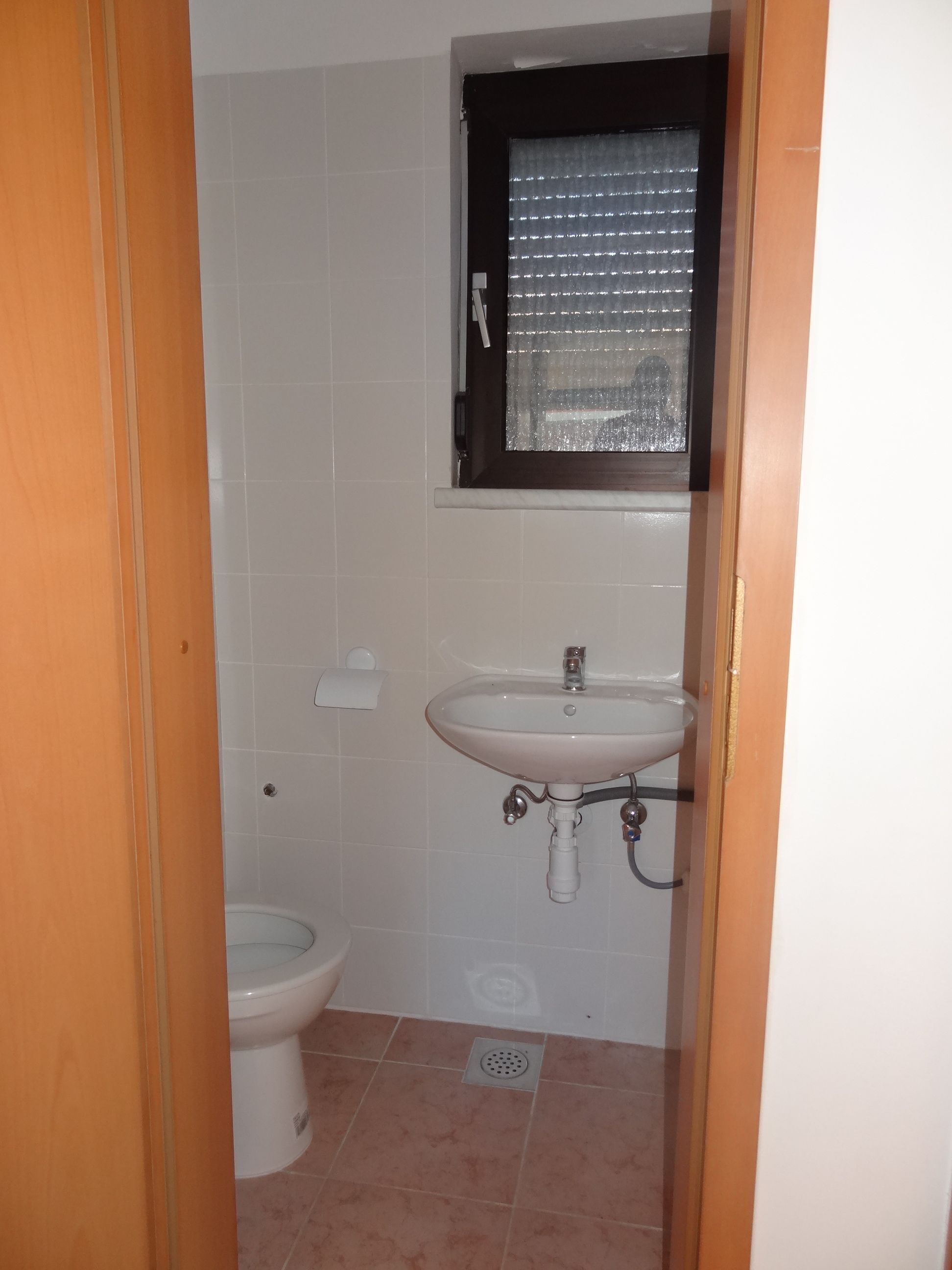 Une salle de bain avec des toilettes, un lavabo et une fenêtre avec des stores.