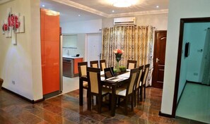 A dining area with a table set for six, flanked by chairs, and a kitchen area with a dishwasher and sink. - St Georgess Height-room With Balcony (Nsawam)
