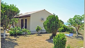 Une maison avec un toit en tuiles, un petit jardin avec différentes plantes et une chaise dans la cour.