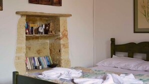 Une chambre avec une cheminée en pierre, un lit avec une literie blanche et une tête de lit en bois.