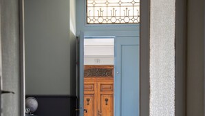 Un couloir au sol à carreaux menant à une porte en bois surmontée d’un panneau de verre décoratif.