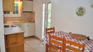 A compact kitchen with a sink, stove, and wooden cabinets. There is a dining table with a polka dot tablecloth and chairs. A wicker basket is on the table.