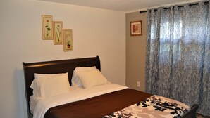 A neatly made bed with a dark headboard, a floral-patterned bedspread, and three framed botanical prints on the wall. - A Perfect Retreat in Grand Forks (Grand Forks)