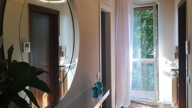 A hallway with a large mirror, a modern light fixture, and a view of a garden through a window. - Room in Apartment - Villa Piera Holiday Home in Cremona Apartment With Independent Entrance (Cremona)