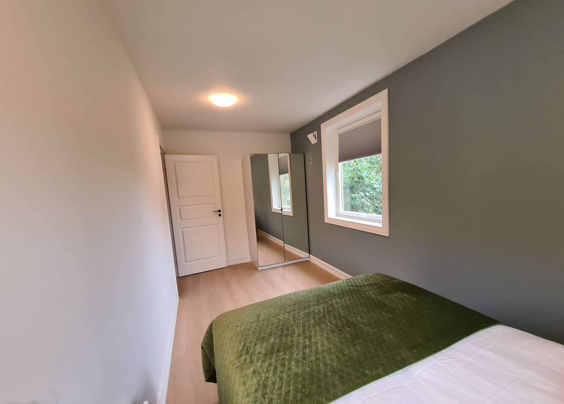 Un dormitorio con cama, ventana, puerta y espejo.