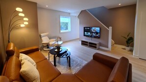 A modern living room with a brown leather sofa, a coffee table, and a TV mounted on the wall. - Spacious And Modern 3-bedroom Near Center, Free Parking (Stavanger)
