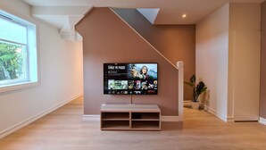 A modern living room with a large flat-screen TV mounted on a wall, a wooden bench in front, and a staircase with a brown accent wall. - Spacious And Modern 3-bedroom Near Center, Free Parking (Stavanger)