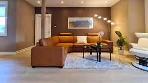 A modern living room with a brown leather sectional sofa, a white armchair, a round coffee table, and a floor lamp. - Spacious And Modern 3-bedroom Near Center, Free Parking (Stavanger)