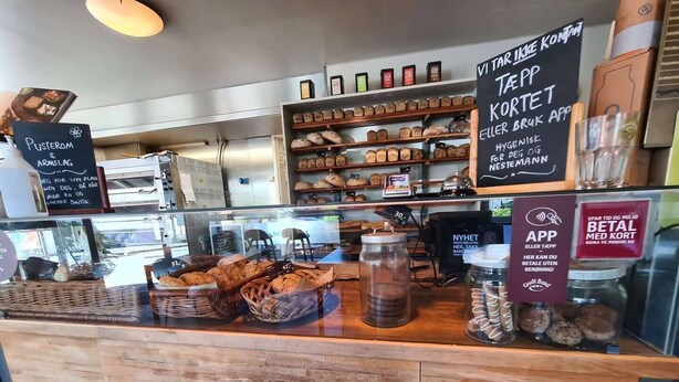 A bakery counter with various baked goods displayed in baskets and jars, a chalkboard menu, and a sign promoting a mobile app. - Spacious And Modern 3-bedroom Near Center, Free Parking (Stavanger)