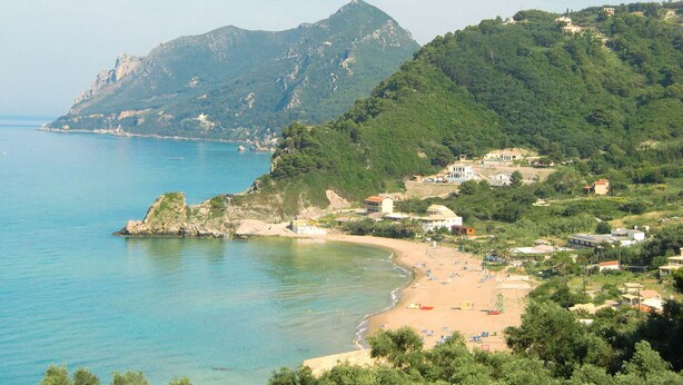 Eine Küstenlandschaft mit Strand, Felsen und Bergen im Hintergrund.