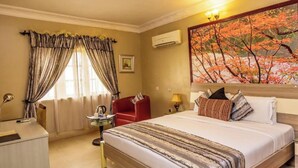 Een hotelkamer met een bed, een bureau, een stoel, een schilderij en een airconditioner.