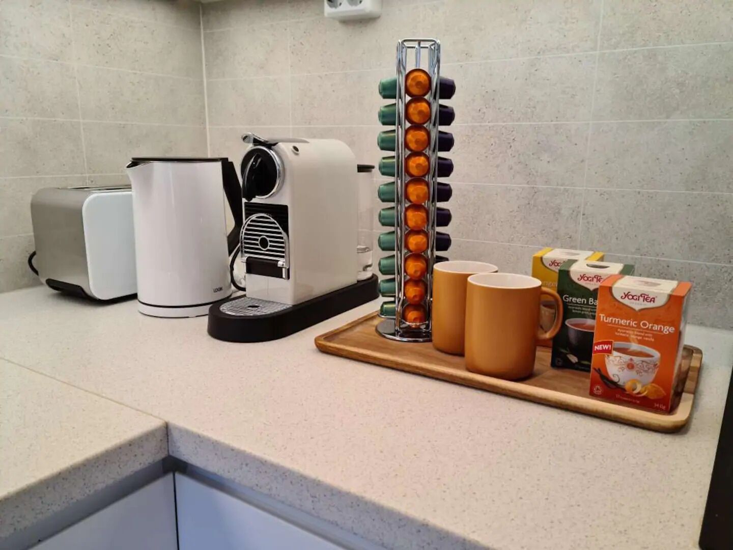 A kitchen counter with a coffee maker, a toaster, a tea infuser, and a tray with tea boxes and cups.