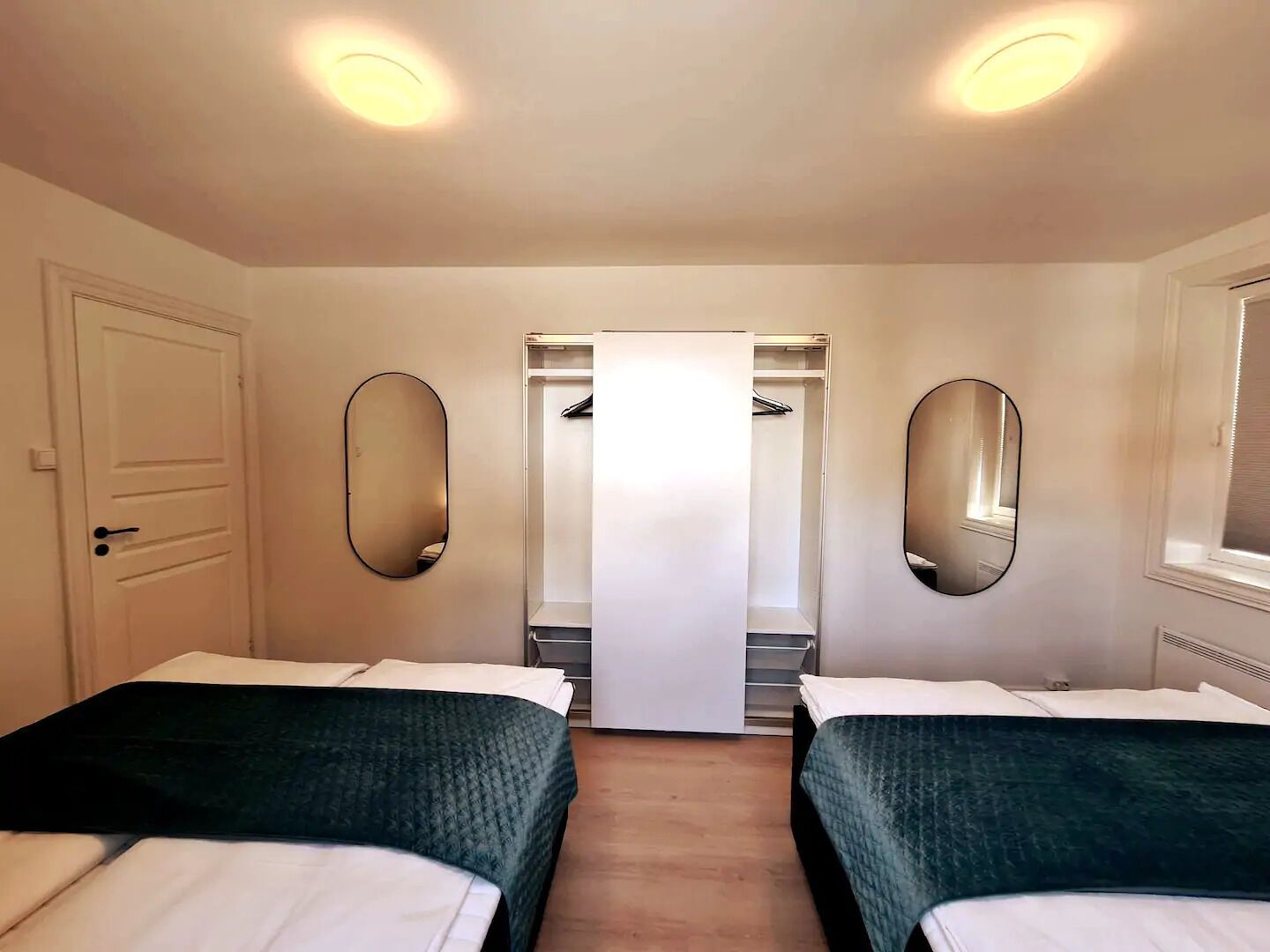 A hotel room with two beds, a wardrobe, and two mirrors.