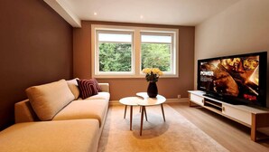 A living room with a beige sofa, a small white table, and a TV on a wooden stand. - Bright And Modern Apartment Near Center, 85 M2, Fully Equipped, Free Parking (Stavanger)